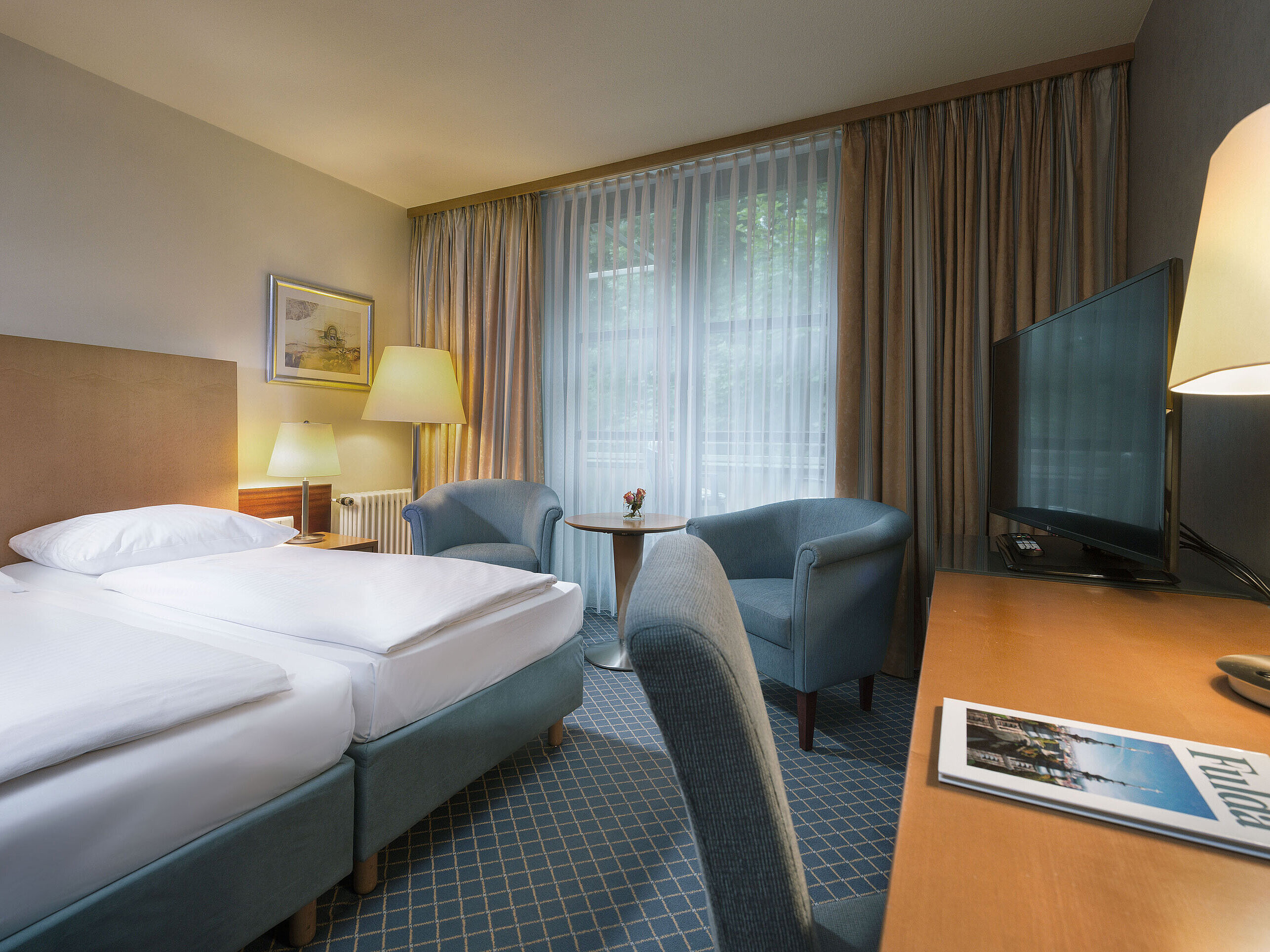 Habitación doble cómoda en el Maritim Hotel Fulda con mobiliario moderno, escritorio y acogedora zona de estar.