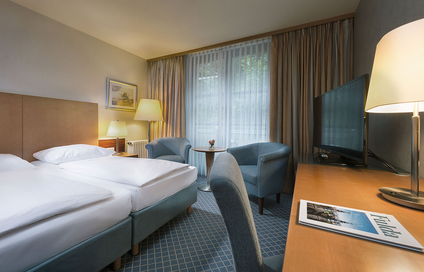 Habitación doble cómoda en el Maritim Hotel Fulda con mobiliario moderno, escritorio y acogedora zona de estar.