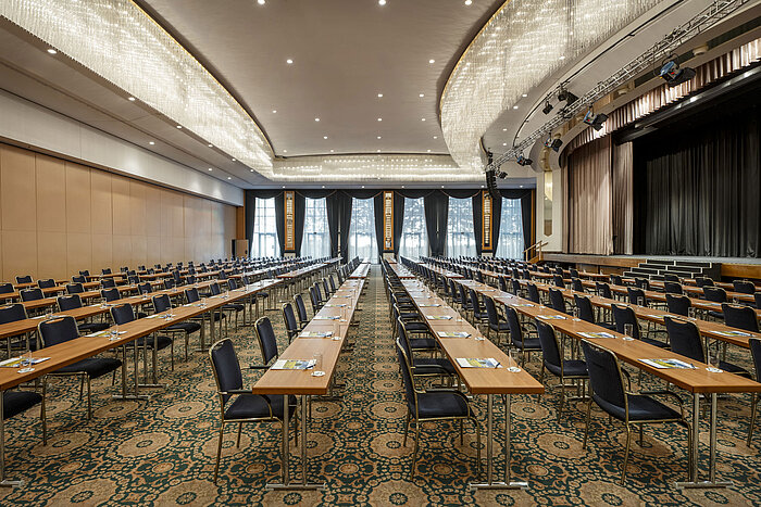 Salón magnífico en el Maritim Hotel Magdeburg con escenario, asientos en fila y lujosa lámpara de araña.