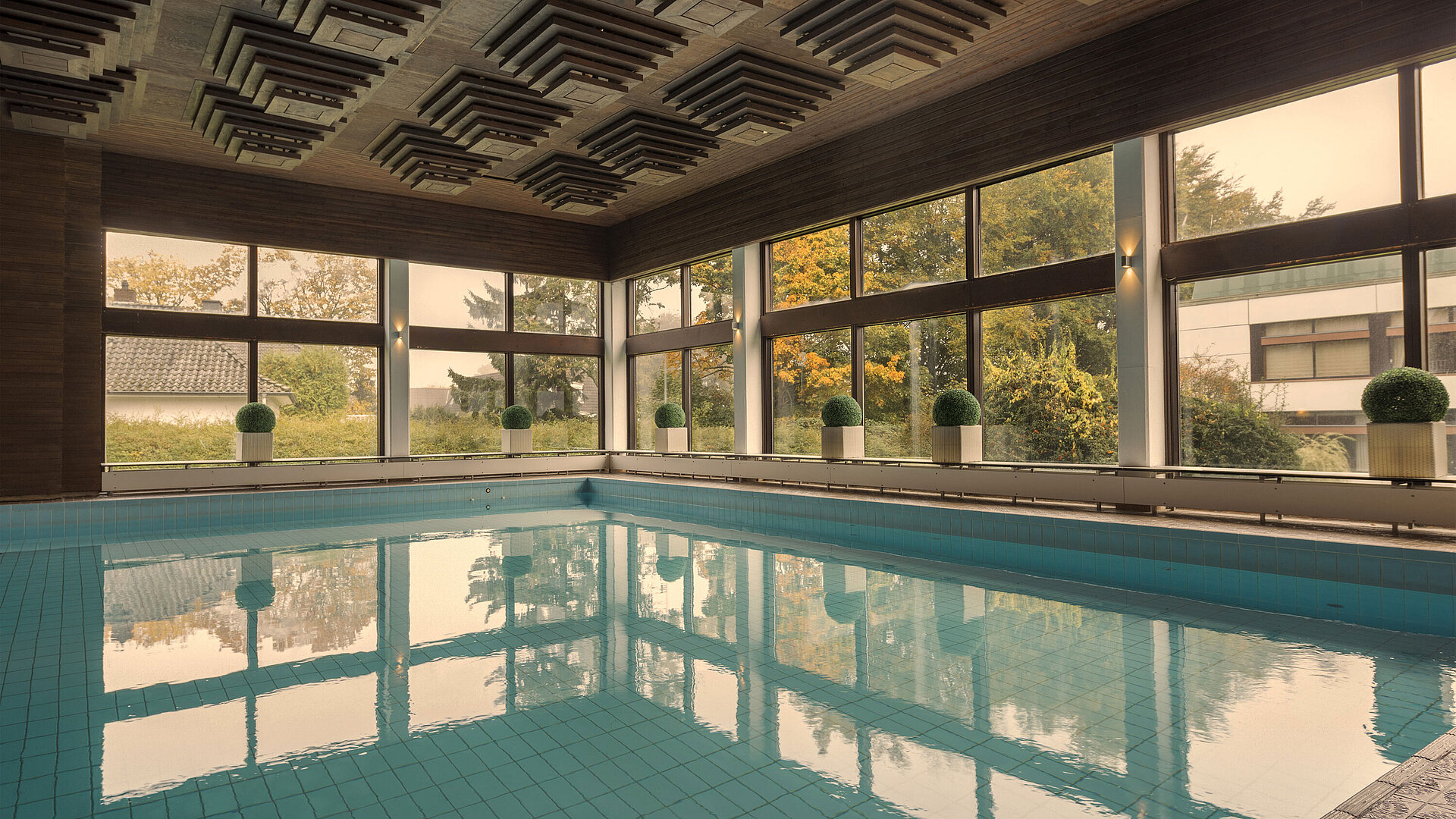 Pool Indoor pool at the Maritim Hotel Kiel, surrounded by large windows offering a view of the greenery.