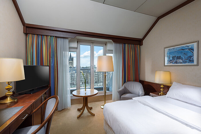 Camera Classic al Maritim Hotel Colonia con letto matrimoniale, scrivania e vista sul Reno e il centro storico.