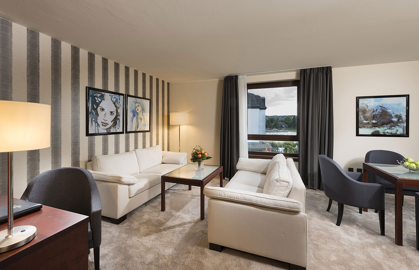 Suite spacieuse avec canapés élégants, table à manger et vue panoramique sur le Rhin au Maritim Hotel Königswinter.