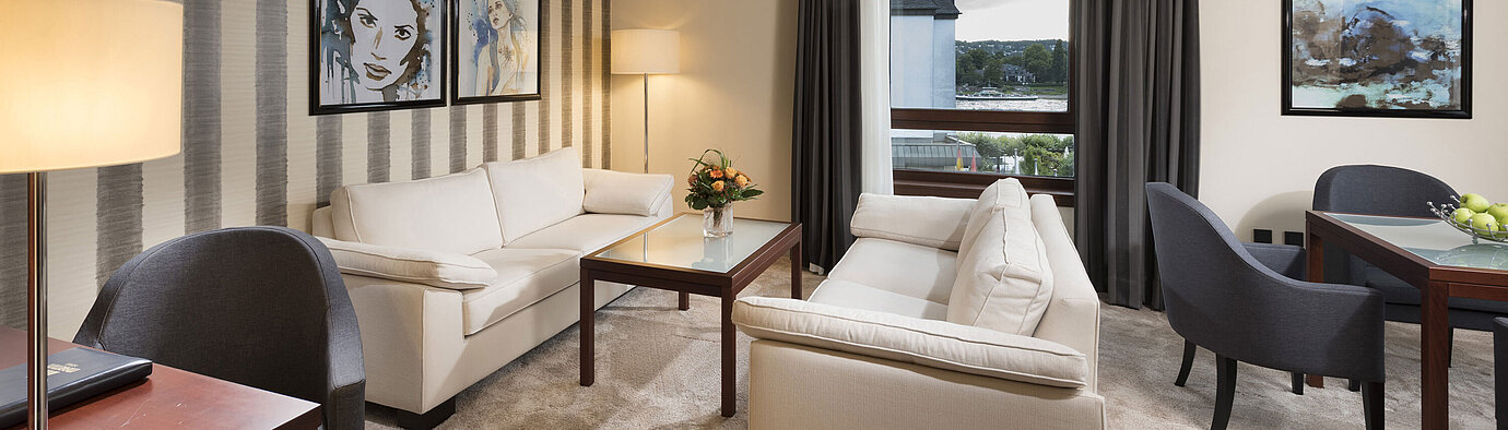 Suite spacieuse avec canapés élégants, table à manger et vue panoramique sur le Rhin au Maritim Hotel Königswinter.