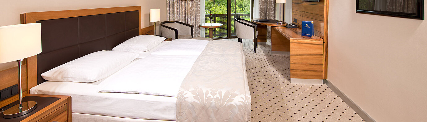 Camera Comfort Camera luminosa all'hotel Maritim Bad Homburg con letto accogliente, scrivania e balcone con vista sul verde.