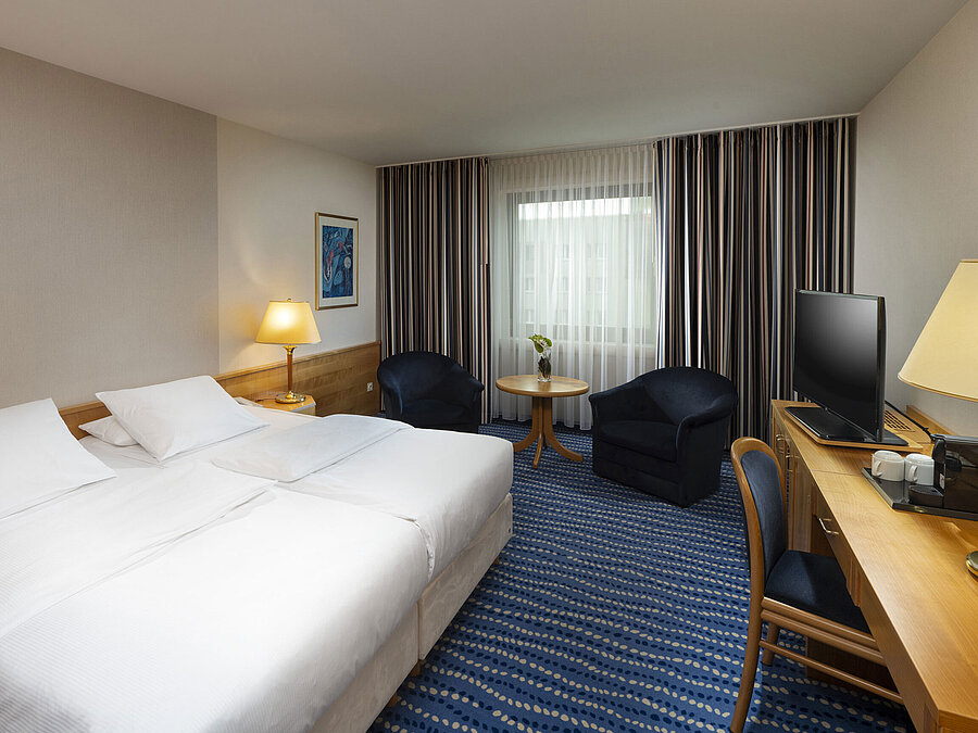 Large bed with bedside tables and lamps, next to seating area and desk.