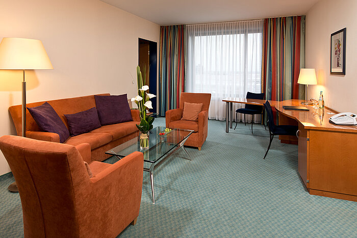 Junior suite spaziosa al Maritim Hotel Frankfurt con area salotto accogliente, scrivania e design luminoso caldo.