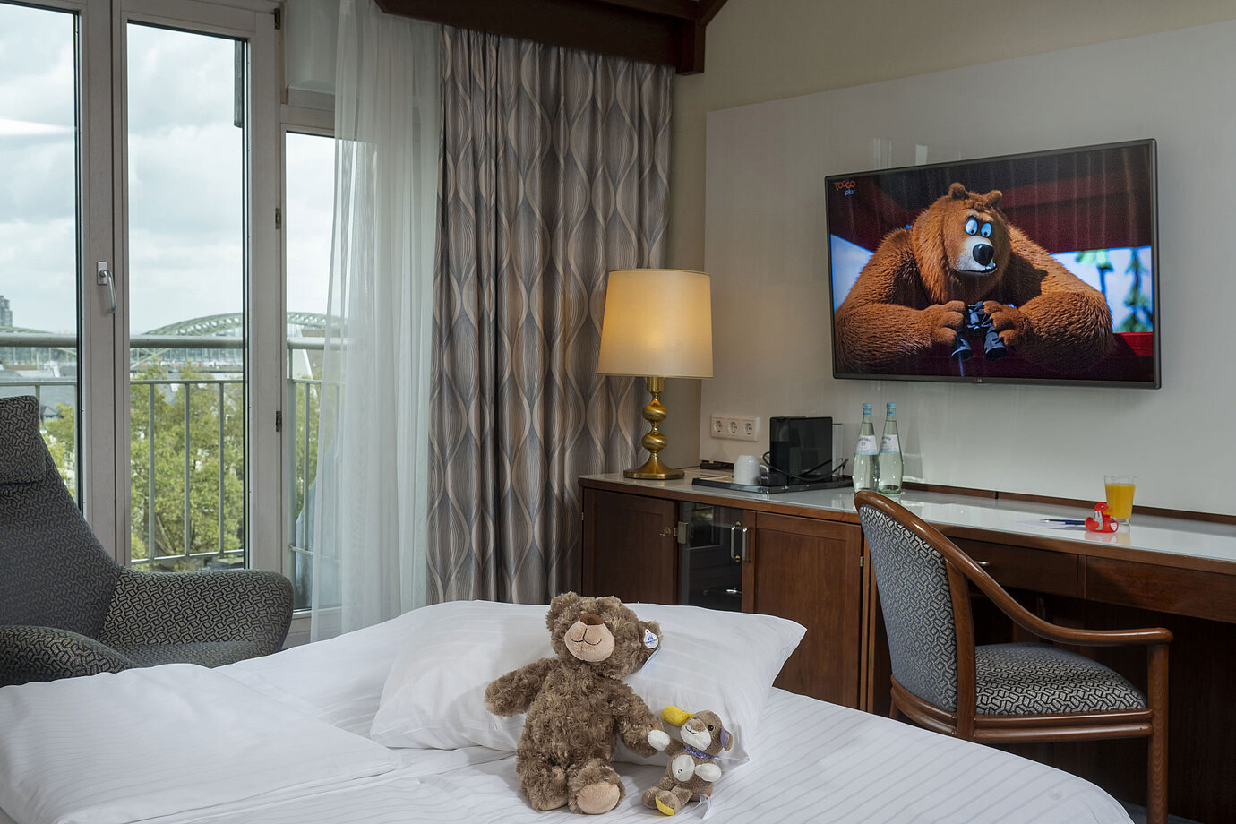 Camera familiare presso l'Hotel Maritim Colonia con TV, peluche sul letto e vista sul Reno.