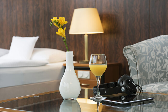 Détail de la chambre Détails d'une chambre du Maritim Hotel Kiel : un verre de jus d'orange, des écouteurs et un vase sur la table, un lit en arrière-plan.