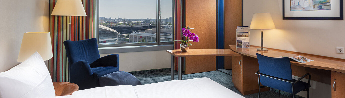 Chambre familiale Confort du Maritim Hotel Frankfurt avec lit double, bureau, rideaux colorés et vue sur la ville.