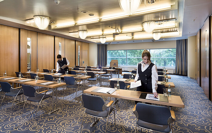 Il personale prepara una sala conferenze al Maritim Hotel Frankfurt con posti a sedere in fila e vista sul verde.