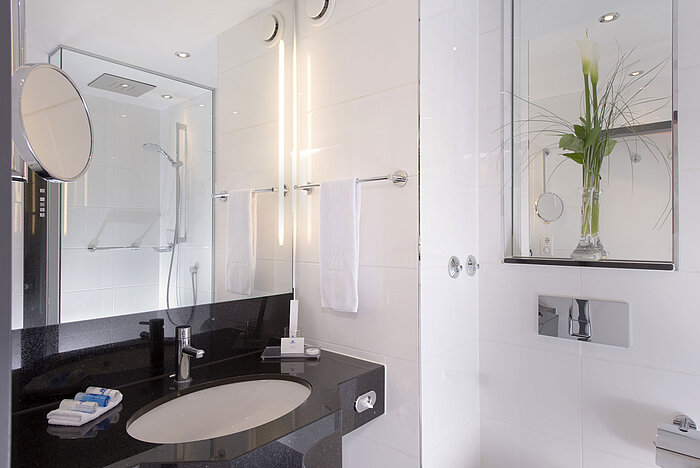 Bagno luminoso con doccia in vetro, specchio e piano nero al Maritim Hotel Monaco