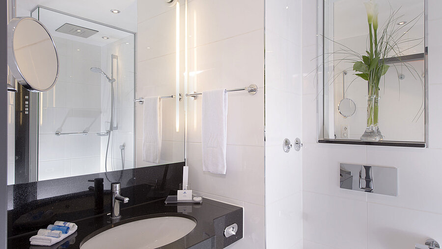 Salle de bain lumineuse avec douche en verre, miroir et plan noir à l’hôtel Maritim Munich