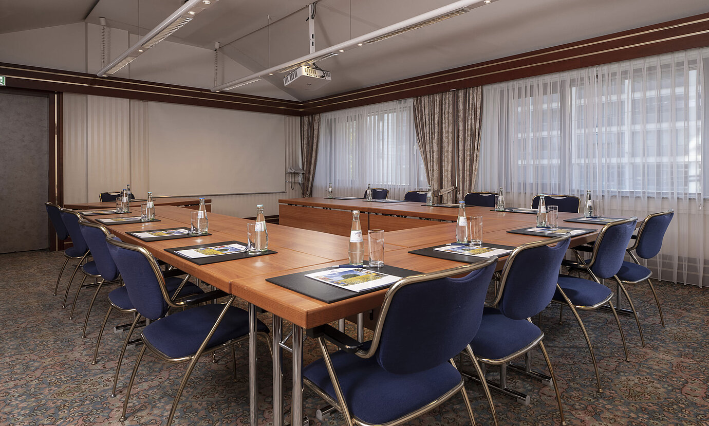 Sala de conferencias moderna en el Maritim Hotel Magdeburg con disposición en forma de U, luz natural y equipamiento de calidad.