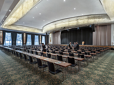 Salón magnífico en el Maritim Hotel Magdeburg con escenario, asientos en fila y lujosa lámpara de araña.