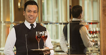 Camarero con dos copas de vino rosado en bandeja en el Maritim Hotel Stuttgart, amable y profesional