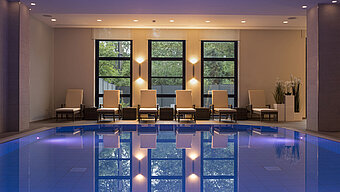 Área de piscina del Hotel Maritim Bonn con elegantes tumbonas e iluminación calmante para una relajación total.
