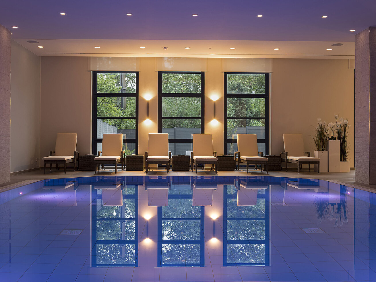 Area piscina dell'hotel Maritim Bonn con lettini eleganti e illuminazione rilassante per un relax totale.