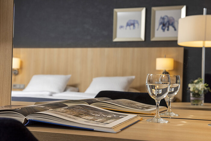 Accogliente camera Comfort al Maritim Hotel Würzburg con specchio, libro illustrato aperto e bicchieri d’acqua