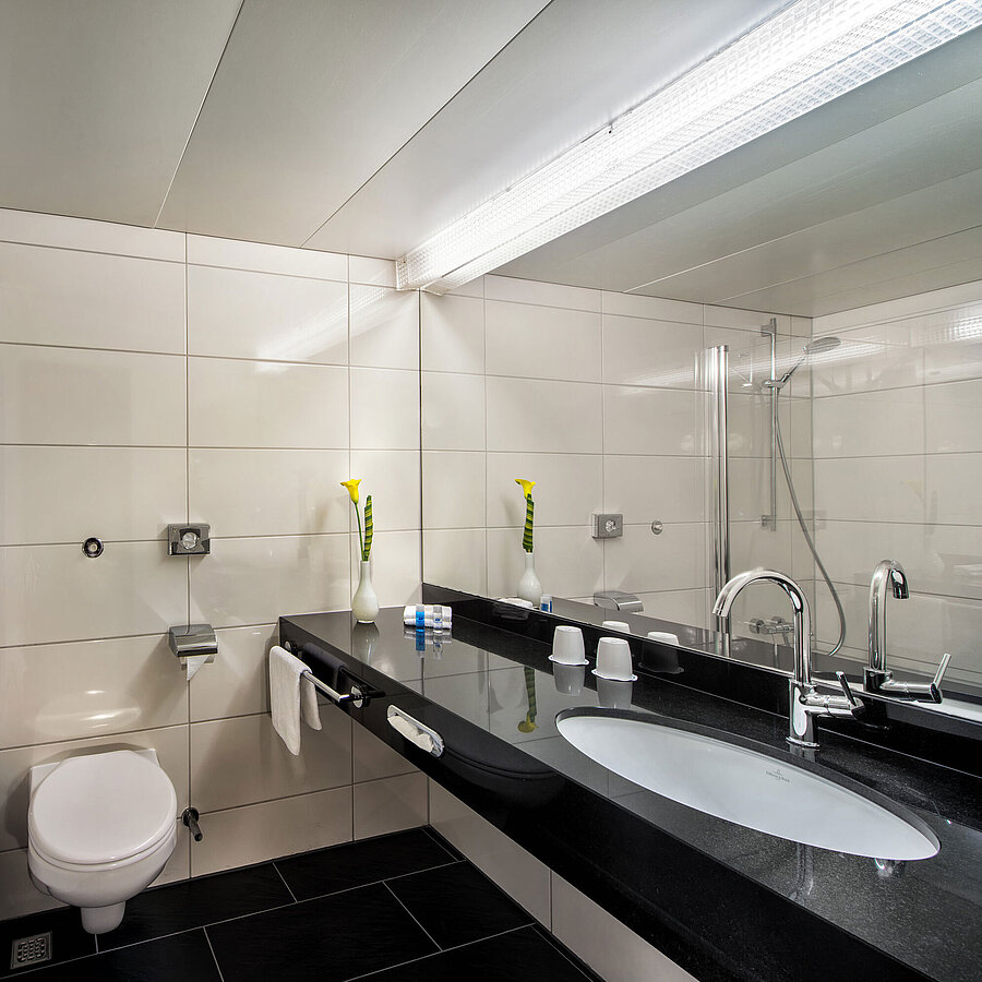 Bathroom at the Maritim Hotel Kiel with bathtub, glass shower screen, washbasin and large mirror on a black shelf.