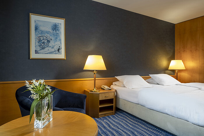 Chambre d'hôtel avec lit double, coin salon confortable et fleurs sur la table, ambiance idéale pour se détendre