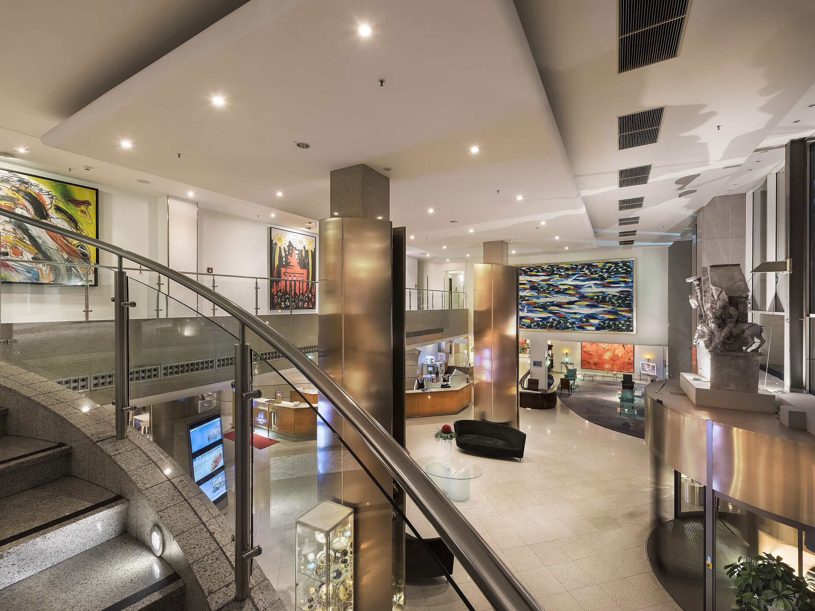 Spacious, modern lobby of the Maritim proArte Hotel with artworks, curved staircase, and elegant interior.
