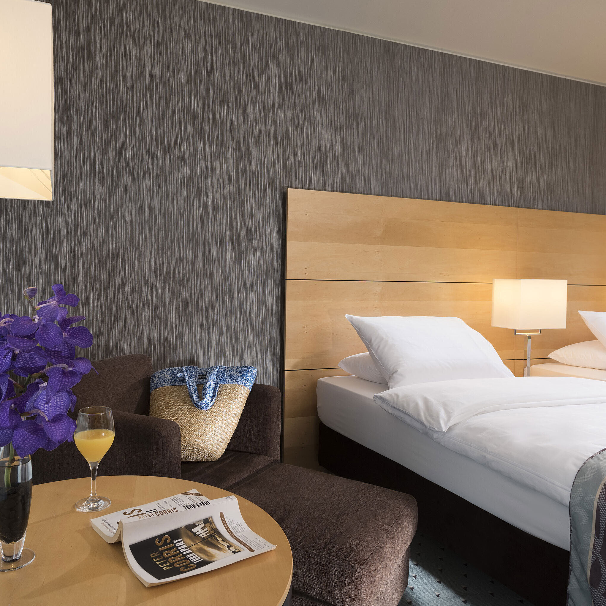Classic room at Maritim Hotel Düsseldorf with elegant double bed, cozy seating area, fresh flower, and reading material.