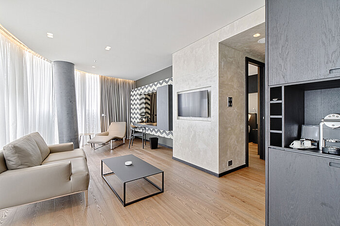 Salon avec canapé, TV, miroir design et fauteuil au Maritim Hotel Plaza Tirana, baigné de lumière