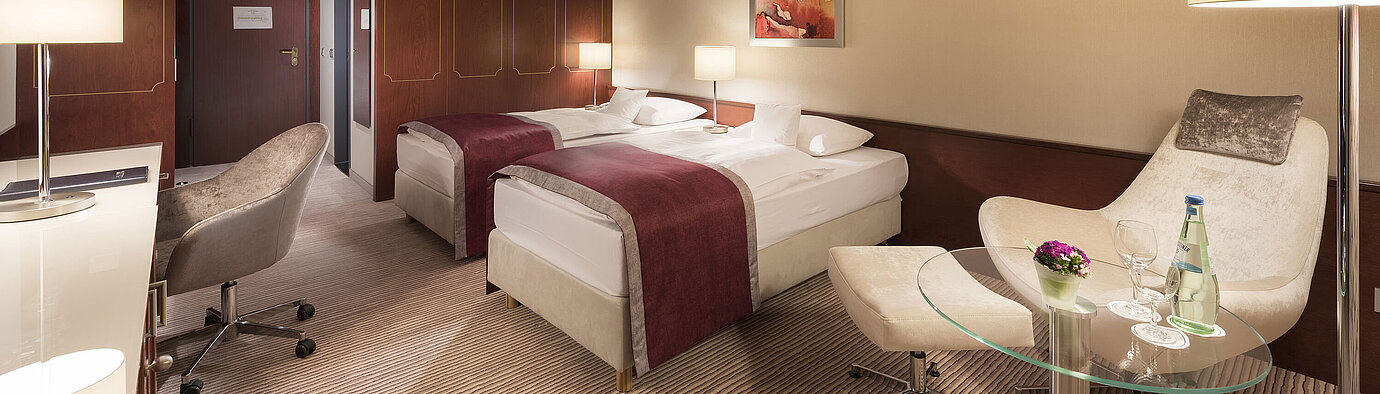 Comfort room  Comfort room at Maritim Hotel Bonn, featuring two single beds, armchair, desk, and modern lighting.