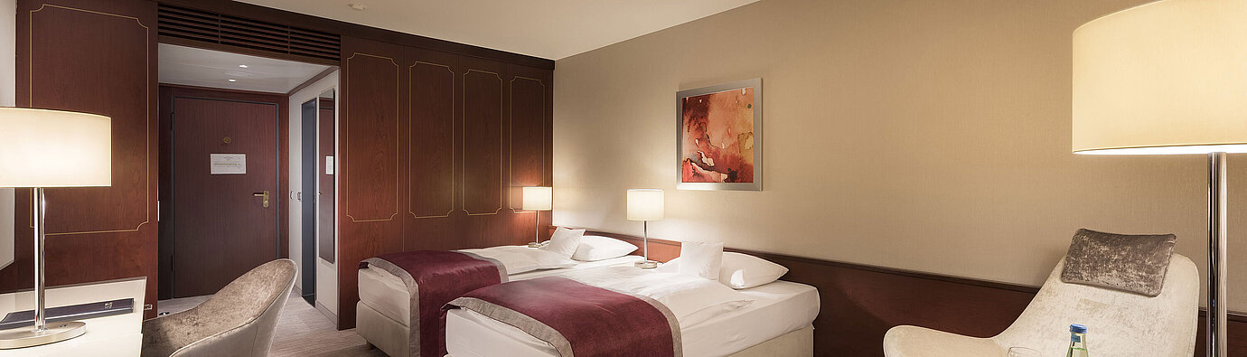 Camera comfort al Maritim Hotel Bonn, dotata di due letti singoli, poltrona, scrivania e illuminazione moderna.