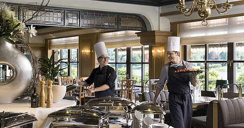 Deux chefs au buffet du Maritim Hotel Königswinter préparent des plats fraîchement disposés avec vue sur le Rhin.
