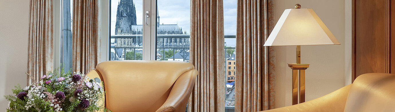 Suite Deluxe  Suite Heumarkt élégante à l'hôtel Maritim Cologne avec fauteuils en cuir confortables et vue directe sur la cathédrale de Cologne.