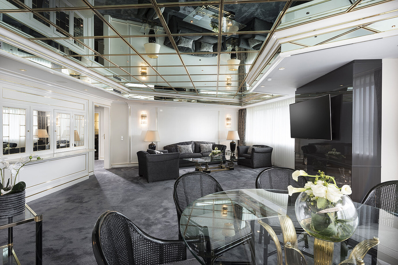 Soggiorno elegante della suite di lusso dell'Hotel Maritim con soffitto a specchio, mobili moderni e grande tavolo da pranzo.