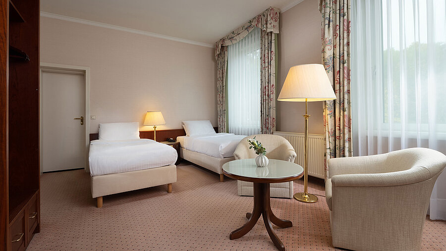 Classic twin room with two beds, seating area, large window and bright traditional design at Maritim Hotel Bad Wildungen.