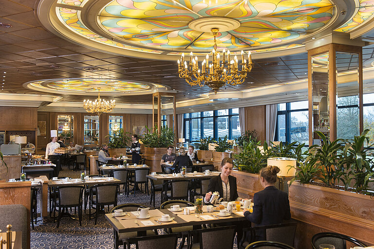 Guests enjoy breakfast in a stylish restaurant with chandeliers and large windows at Maritim Hotel Hannover.