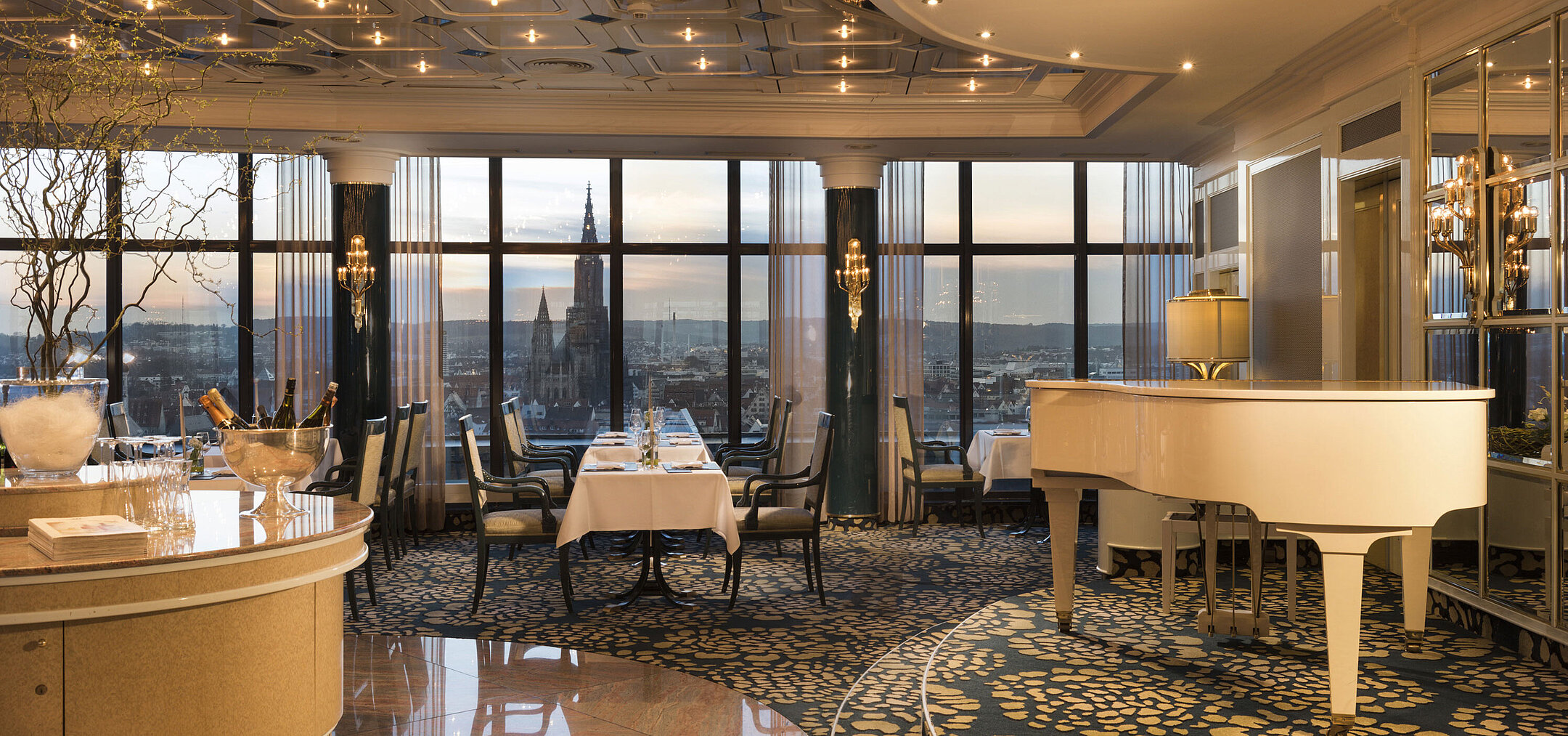Restaurante panorámico elegante con piano y vista al atardecer de la catedral de Ulm