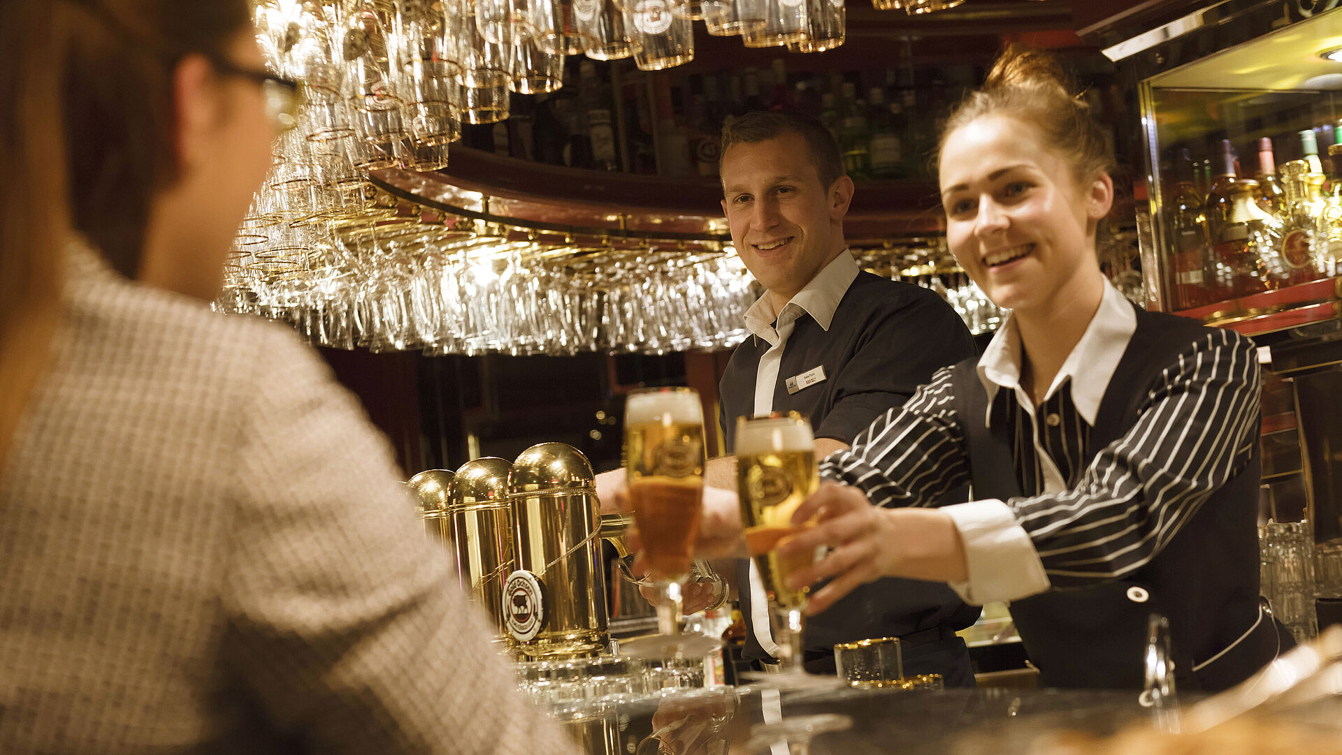 Two staff members serve freshly tapped drinks at the bar at the Maritim Hotel Ulm