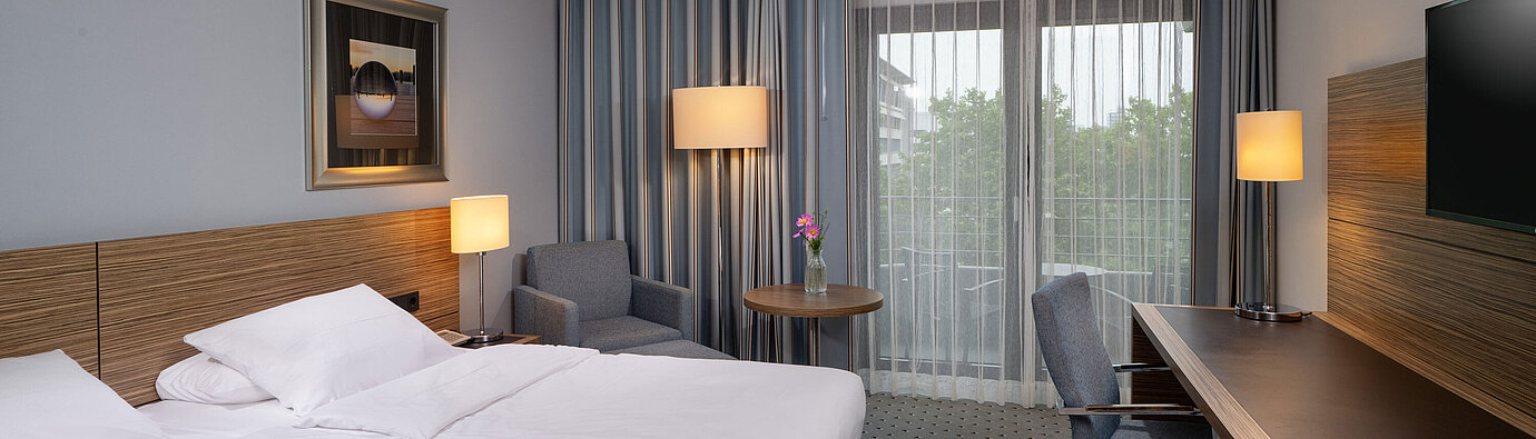 Full view of the Comfort room at the Maritim Hotel Darmstadt with a bed, desk, and balcony access