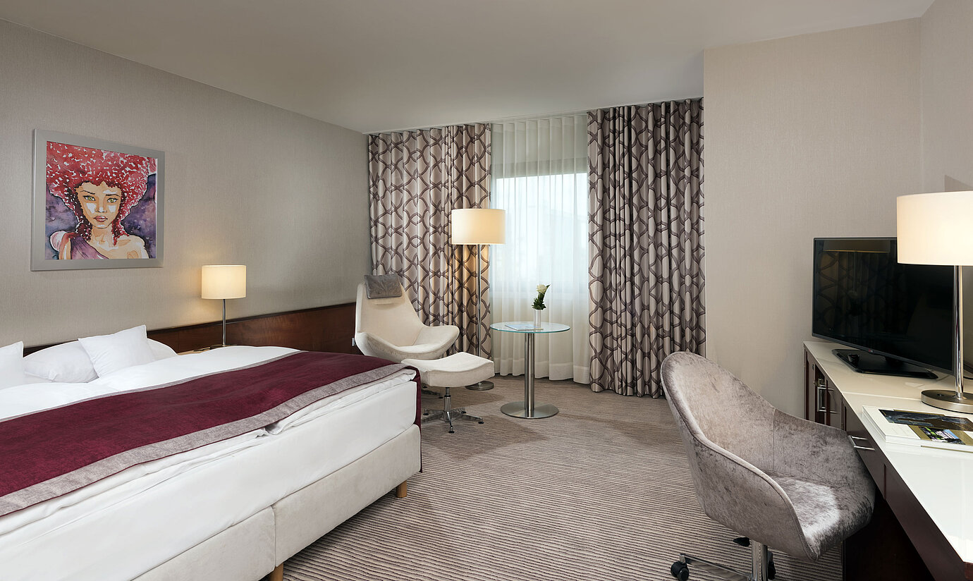 Camera Comfort al Maritim Hotel Bonn con letto accogliente, sedie, scrivania e tende moderne.