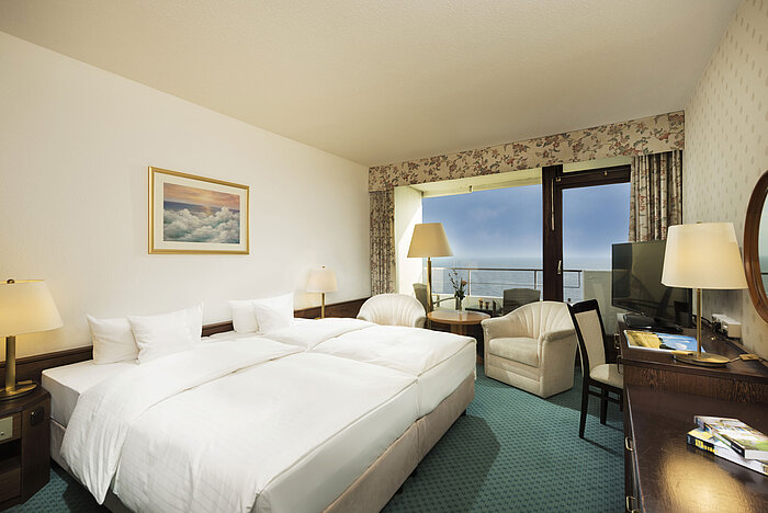Chambre moderne au Maritim Seehotel Timmendorfer Strand avec vue mer depuis le balcon, lit double et coin salon.