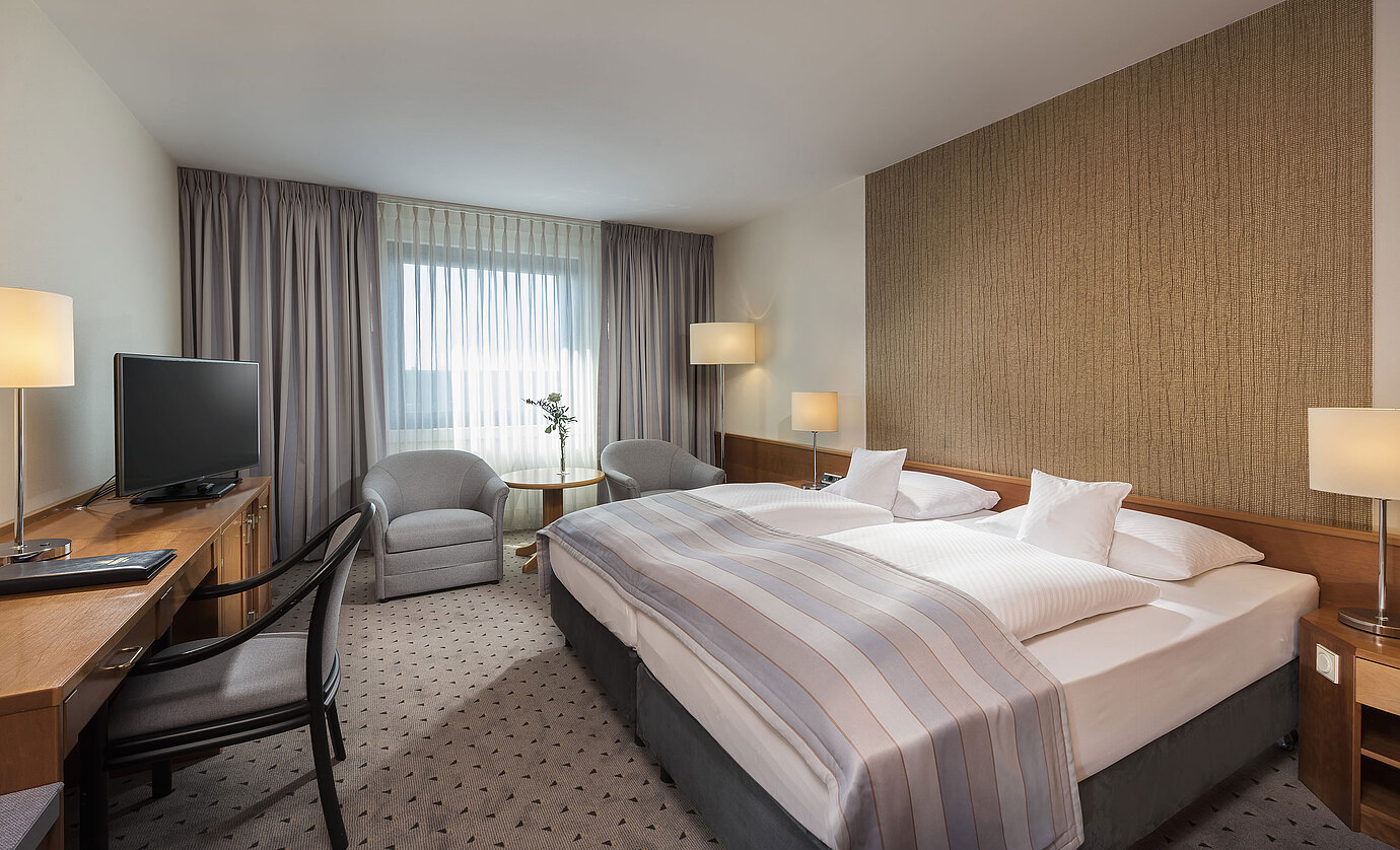 Camera doppia Classic moderna con letto matrimoniale accogliente, area salotto e scrivania al Maritim Hotel Hannover.