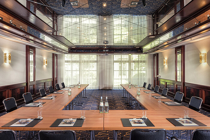 Sala de conferencias elegante con disposición en U, luz natural y techo de espejo.