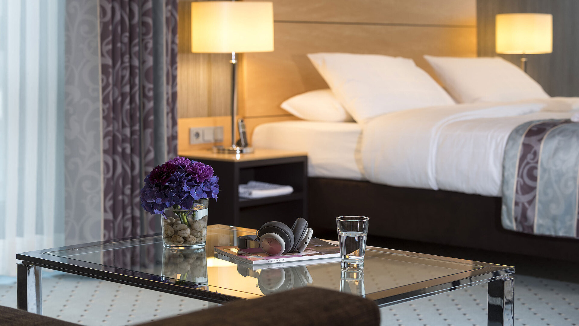 Master Suite Primer plano de la suite principal en el Maritim Hotel Düsseldorf con un vaso, auriculares y flores en una mesa de cristal.