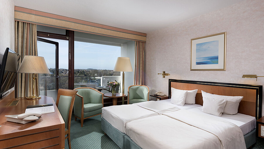 Camera comfort al Maritim Seehotel Timmendorfer Strand con letti gemelli, area salotto, scrivania e balcone con vista.