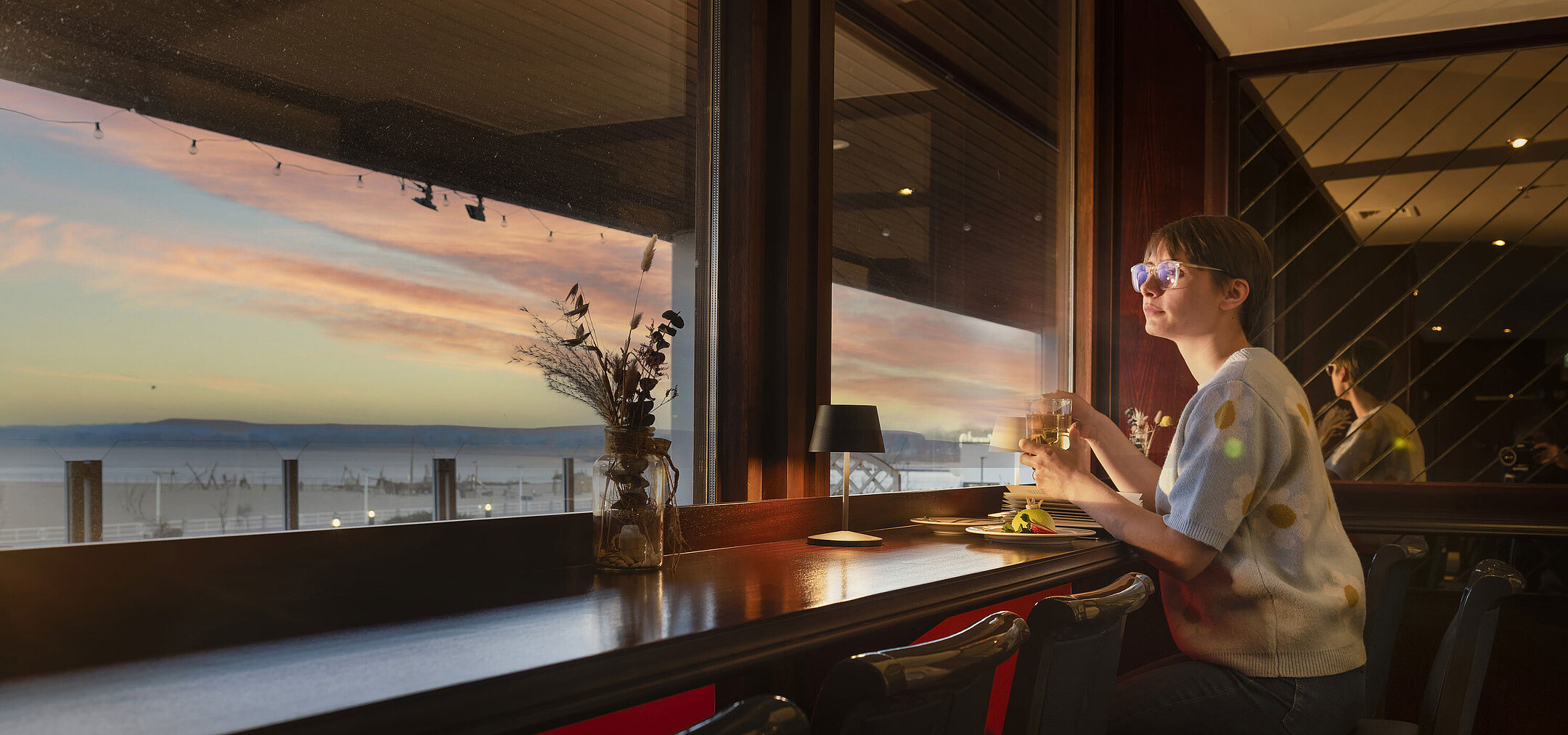 Guest enjoying a drink by the window with a sunset view at Maritim Hotel Travemünde