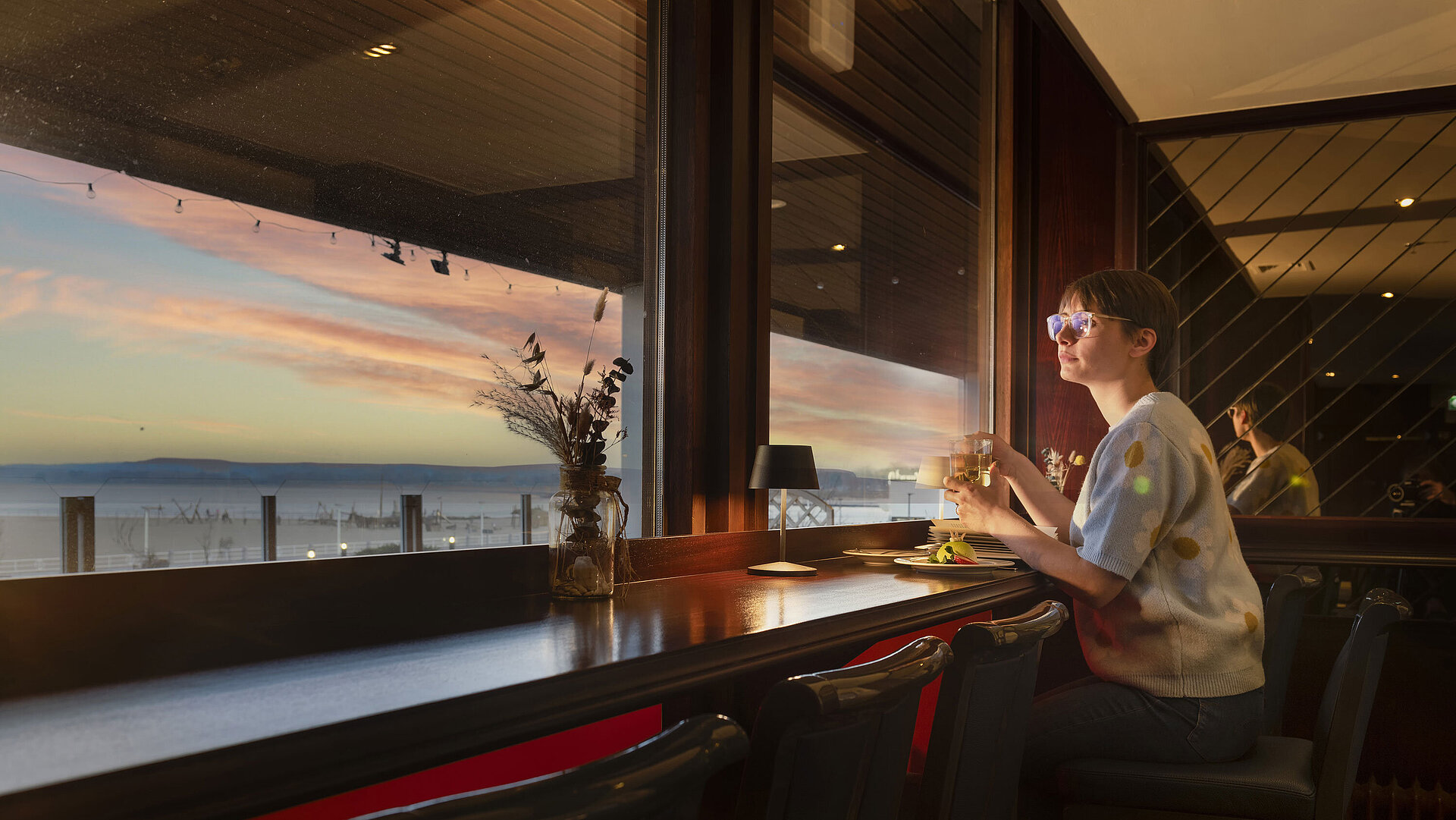Guest enjoying a drink by the window with a sunset view at Maritim Hotel Travemünde