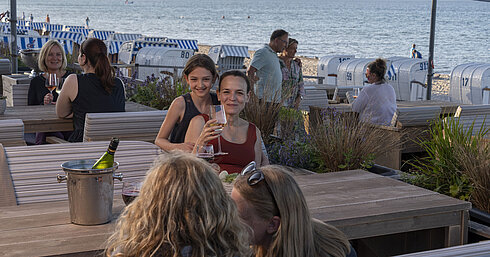 Ospiti che gustano vino al bar sulla spiaggia del Maritim Seehotel Timmendorfer Strand con vista su sdraio e mare.