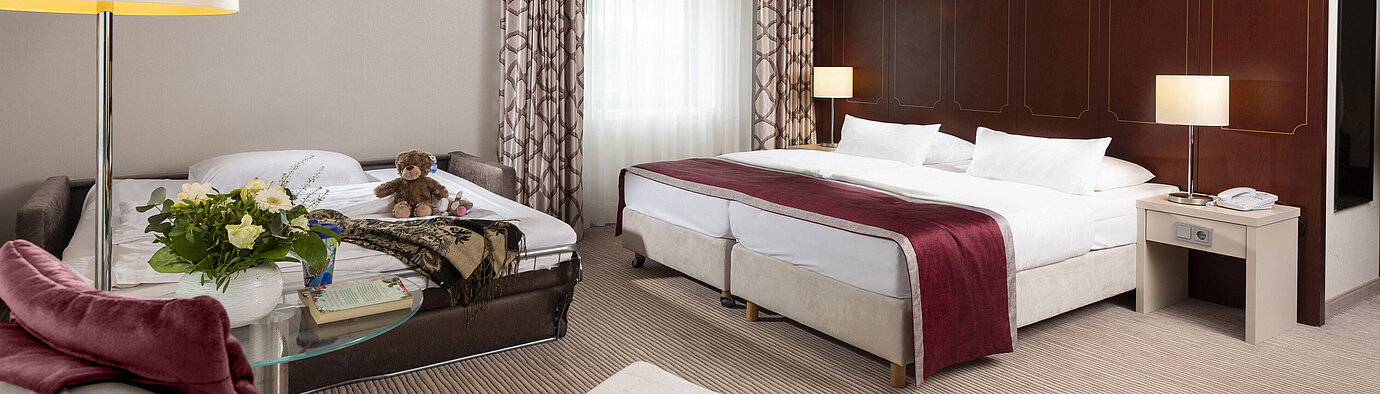 Comfort Family room  Comfort family room at Maritim Hotel Bonn with a large double bed, pull-out sofa, armchair, and flower arrangement.