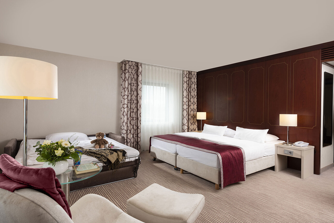 Camera familiare Comfort al Maritim Hotel Bonn con letto matrimoniale, divano letto, poltrona e composizione floreale.