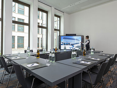 Salle de réunion compacte à l'hôtel Maritim Ingolstadt avec grand écran, technologie moderne et lumière naturelle.