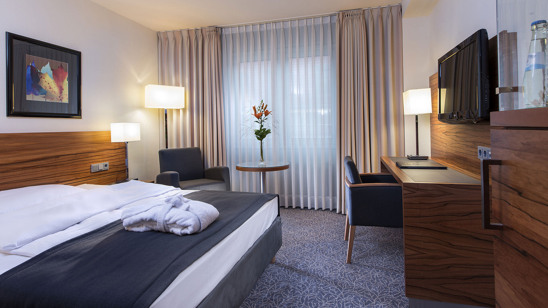 Chambre double moderne à l'hôtel Maritim. Confortablement équipée avec un grand lit, un espace de travail et un fauteuil.